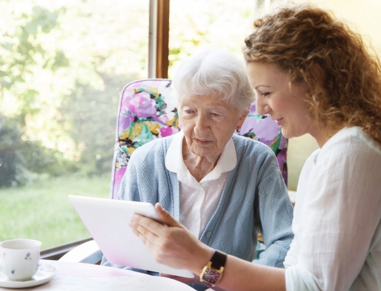 A Staying In Place caregiver and an older woman in St. Louis looking at a tablet together at a sunlit table